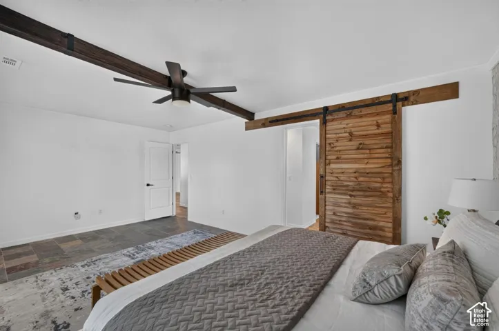 Exposed wood beams, ceiling fan, wood-finish barn door, tiled flooring, white painted walls