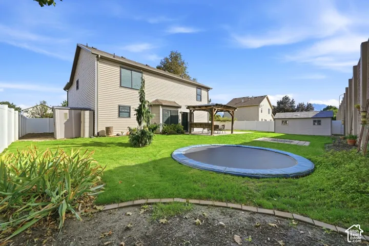 Expansive lawn area with a built-in trampoline, a detached storage shed, a wood pergola, and full privacy fencing