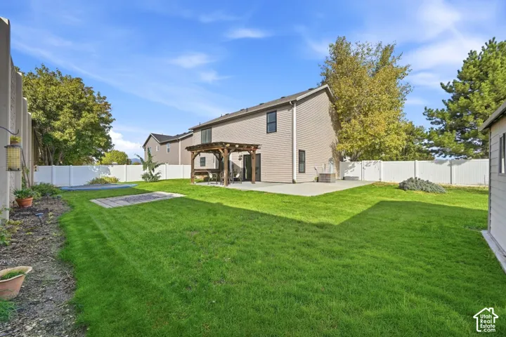 Expansive backyard featuring a manicured lawn, concrete patio, and a wood pergola