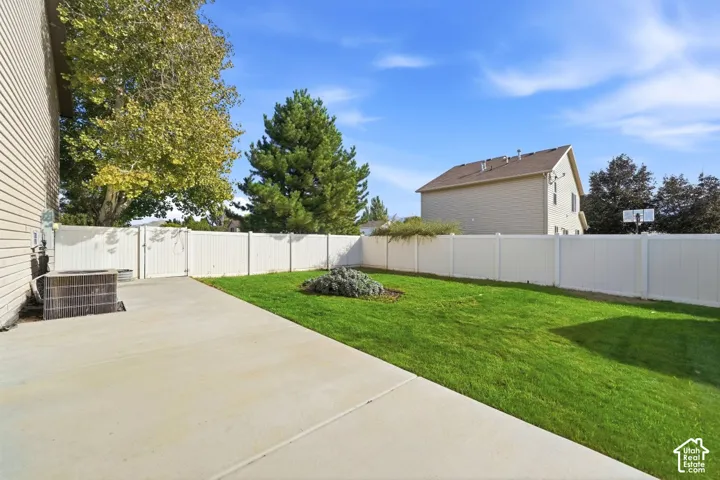 Concrete patio with a manicured lawn, white privacy fencing, and mature trees
