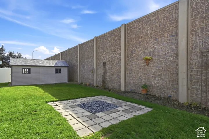 Expansive backyard featuring a manicured lawn, paver patio, and storage shed with a shingle roof