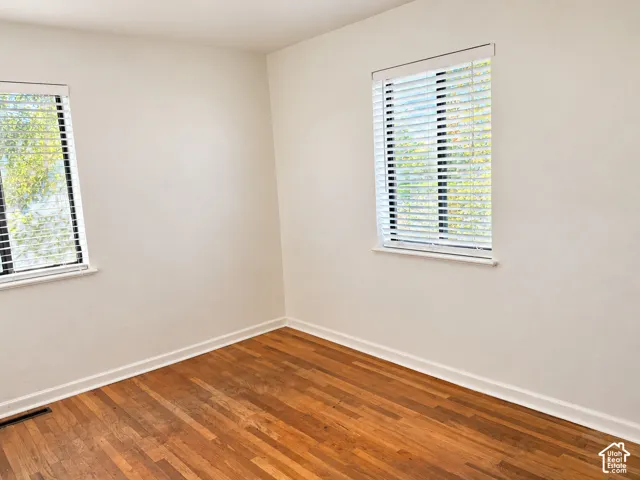 Hardwood flooring, two windows with blinds, and neutral painted walls