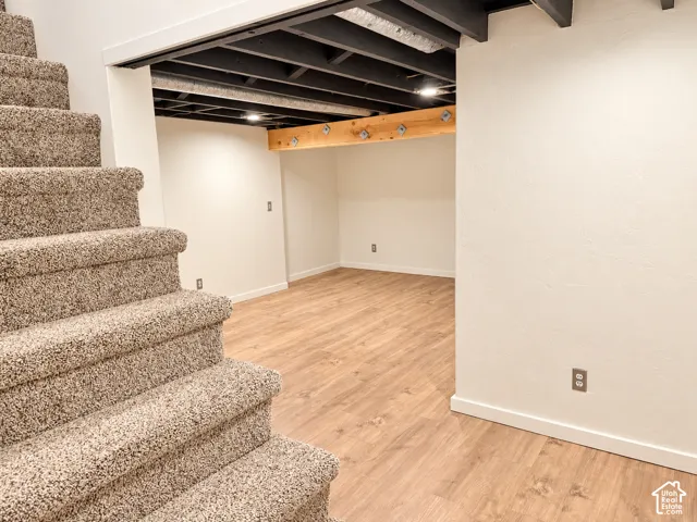 Carpeted staircase with light laminate flooring, white baseboards, and white walls