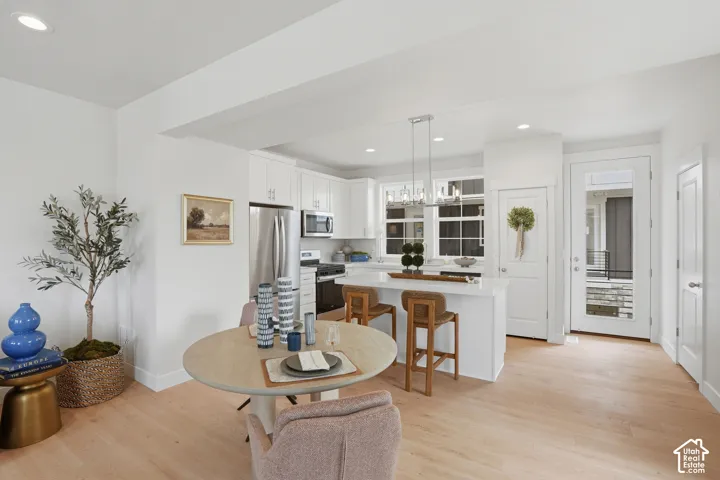 Open-concept living area featuring light wood-finish flooring, white cabinetry, stainless steel appliances, a kitchen island with seating, and recessed lighting