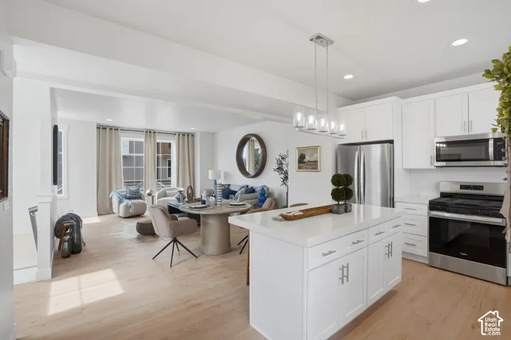 Open-concept living space featuring wood-finish flooring, white shaker cabinetry, stainless steel appliances, a kitchen island with seating, and recessed lighting