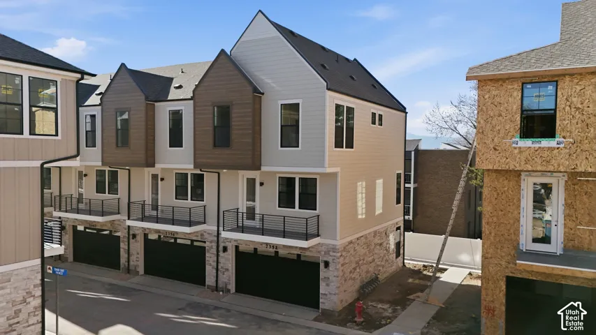 Contemporary townhome with stone-clad lower level, multi-tone siding, black-framed windows, and a private balcony with black railings