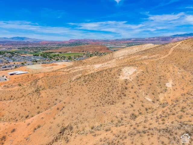 Expansive desert landscape with natural terrain, distant urban development, and remote mountain ranges under a clear sky