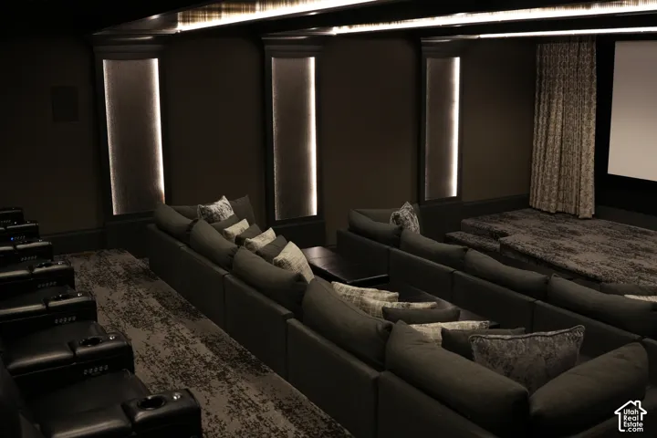 Tiered seating with integrated cup holders, recessed lighting, wall-mounted sound panels, and a large projection screen with a patterned curtain