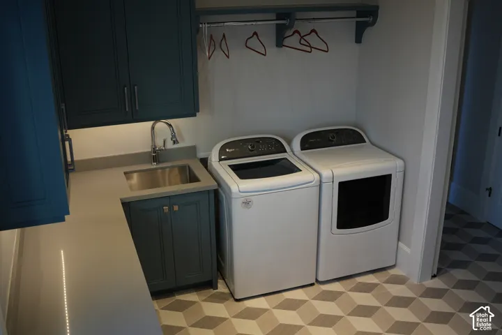Laundry area featuring teal cabinetry, a stainless steel sink, light-toned countertop, and patterned flooring