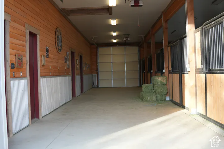 Open-span concrete flooring, wood-paneled walls, multiple stalls with wood and metal construction, and a large overhead door