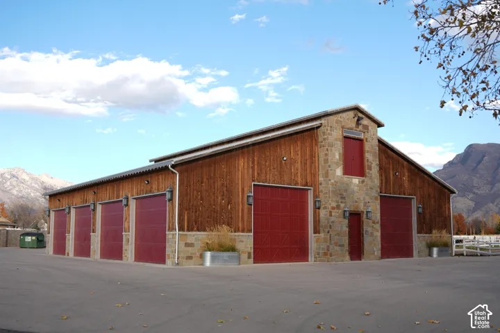 Stone and wood-sided structure featuring multiple red garage doors, prominent exterior lighting, and a white fence