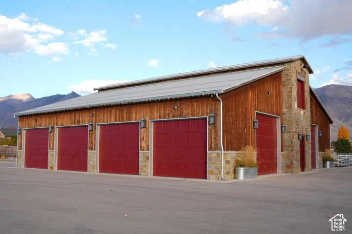 Wood-sided structure featuring a metal roof, stone accents, multiple red garage doors, and exterior lighting fixtures