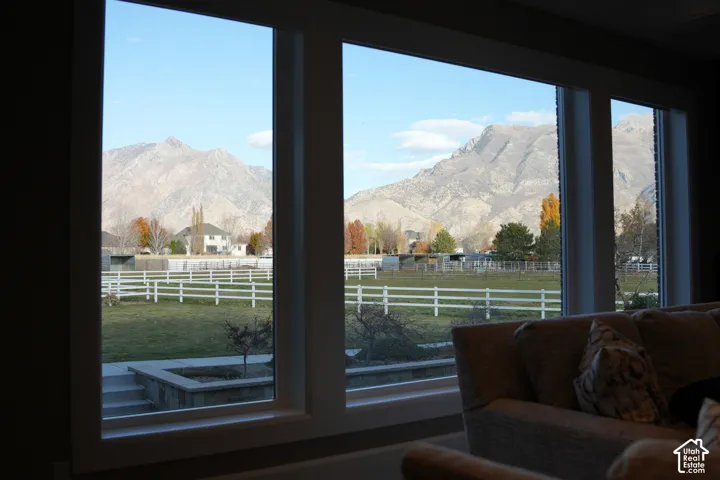 Large windows with white frames frame a mountain backdrop, a green field, and a white fence