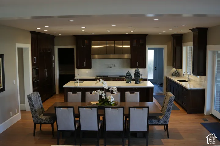 Open-concept kitchen and dining area featuring wood-finish flooring, recessed lighting, dark wood cabinetry, and a center island with a white countertop