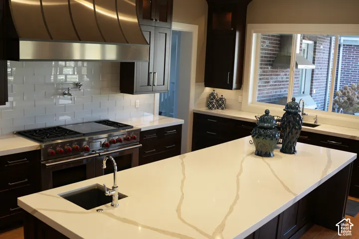 Gourmet kitchen with professional-grade range, stainless steel vent hood, white subway tile backsplash, dark wood cabinetry, and a large central island with an undermount sink