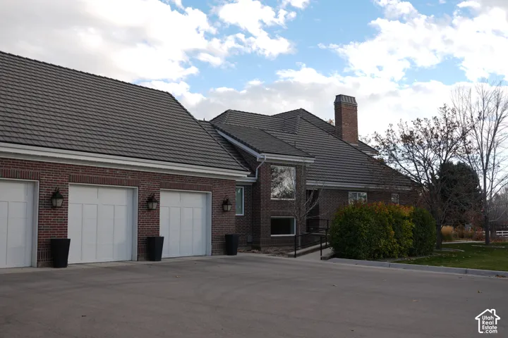 Brick exterior with multiple white garage doors, a tile roof, and a prominent chimney feature