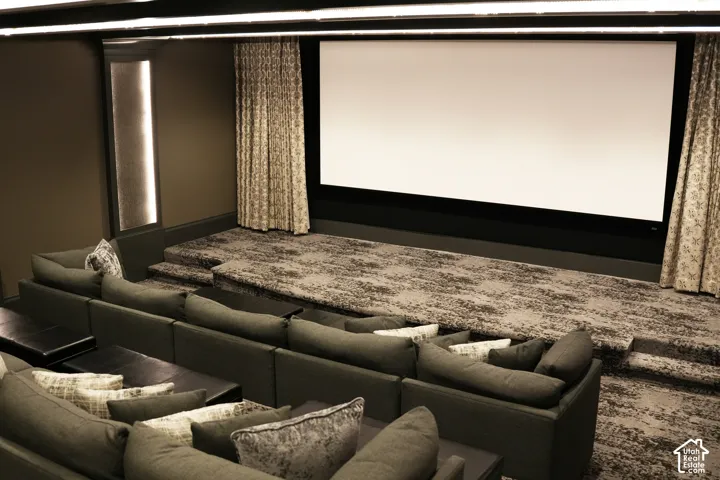 Dedicated media room featuring a large projection screen, tiered seating, patterned wall-to-wall carpeting, and accent lighting