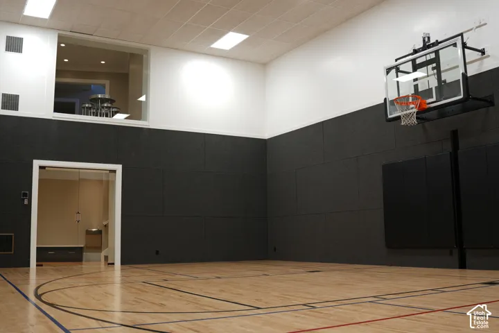 Indoor court with wood-finish flooring, a mounted basketball hoop, and padded wall panels