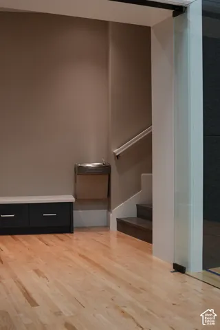 Light wood-finish flooring, built-in dark cabinetry with light countertop, built-in drinking fountain, dark wood-finish stairs, and clear glass partition