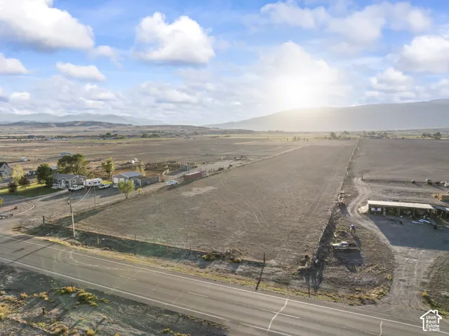 Expansive undeveloped land featuring a paved road frontage, established fencing, and visible mountain scenery