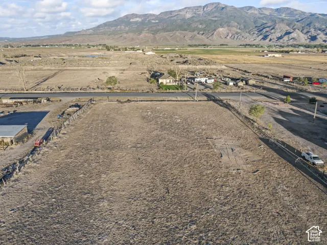 Expansive open land parcel with a perimeter fence, a paved road border, and distant mountain scenery