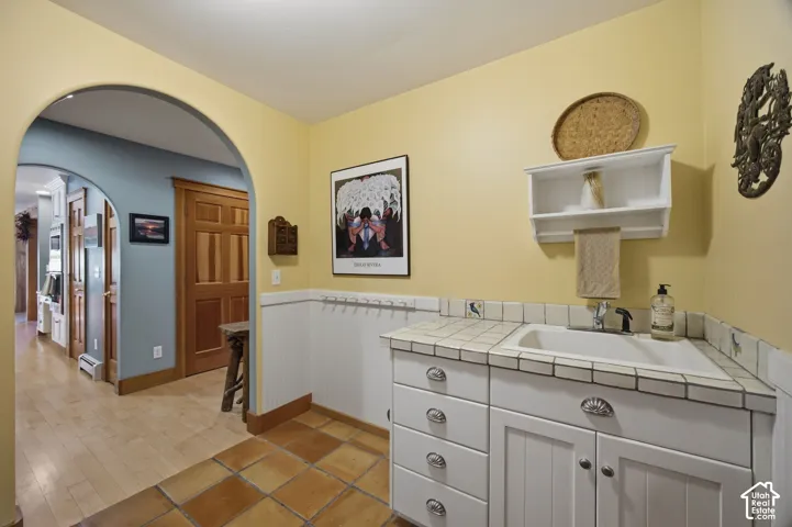 Built-in sink with tiled countertop, wood-finish flooring, recessed wall paneling, and arched doorways