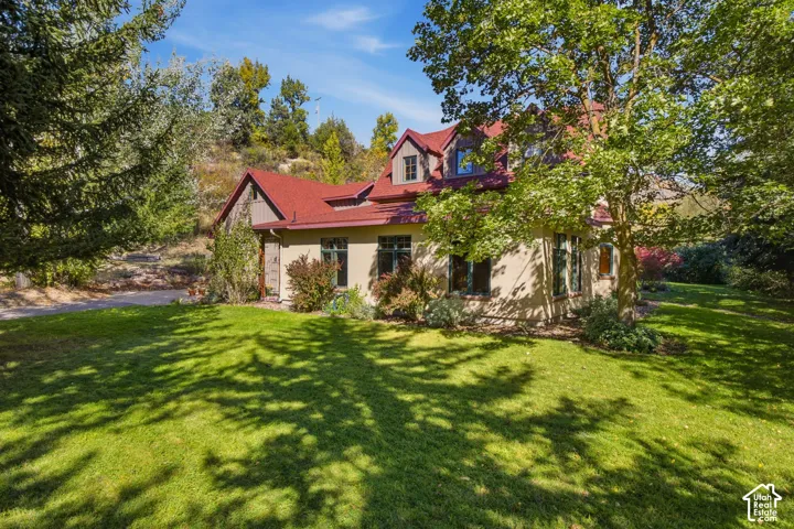 Stucco exterior with a red roof, dormer windows, and a green lawn with mature trees