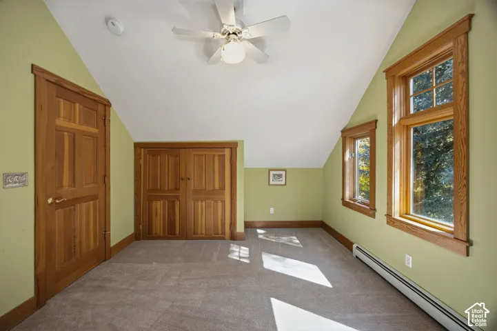 Sloped ceiling room featuring wood doors, two windows with wood trim, a built-in closet, and a ceiling fan