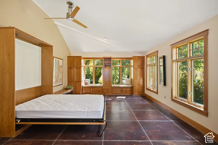 Vaulted ceiling with a ceiling fan, a built-in wall bed, wood-finish flooring, multiple windows with wood trim, and built-in cabinetry with a window seat