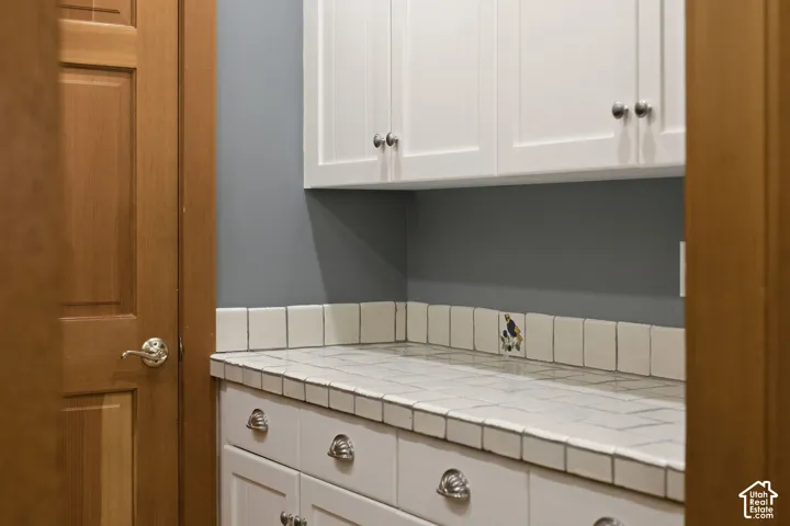 White shaker-style cabinetry with chrome hardware, tile countertop, and a tiled backsplash featuring an accent tile