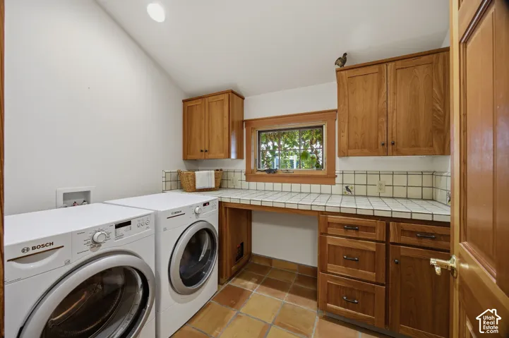 Laundry area featuring ceramic tile flooring, wood cabinetry, a tiled countertop, and a window with wood trim