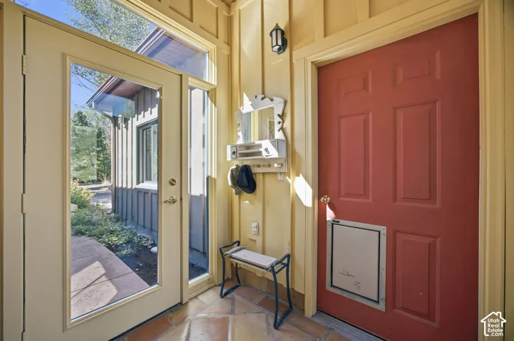 Terracotta-style tile flooring, wood paneling, full-lite entry door, exterior sconce lighting, and a solid panel door