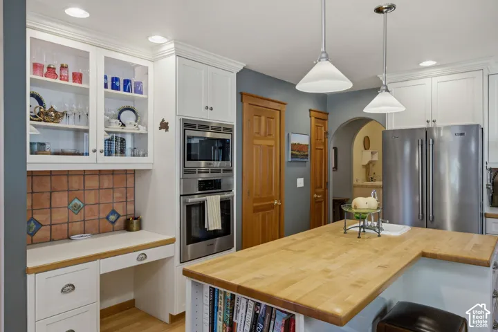 Kitchen featuring a butcher block island, stainless steel appliances, white cabinetry, a built-in desk, and an arched doorway