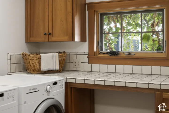 Wood-finish cabinetry, tile countertop, and a wood-framed window