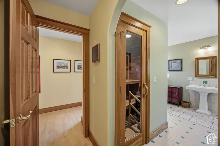 Wood-paneled door with brass hardware, wood-finish flooring, built-in wine storage, pedestal sink with dual faucets, and tiled flooring