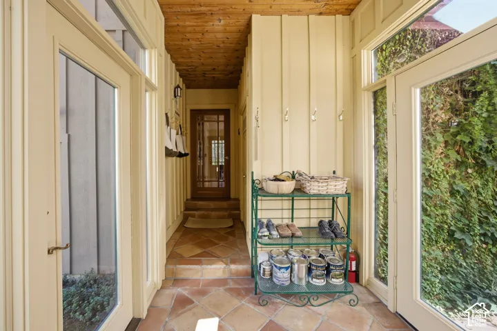 Tiled flooring, wood-paneled ceiling, board-and-batten wall treatment, French doors with transom windows, and a solid wood door with glass panes