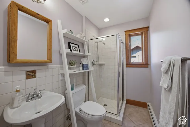 Pedestal sink with chrome fixtures, wood-framed mirror, white subway tile wainscoting, glass-enclosed shower with white tiled walls, and a wood-trimmed window