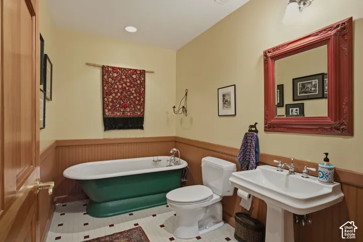 Pedestal sink with chrome fixtures, wainscoting, a freestanding bathtub, and square floor tiles