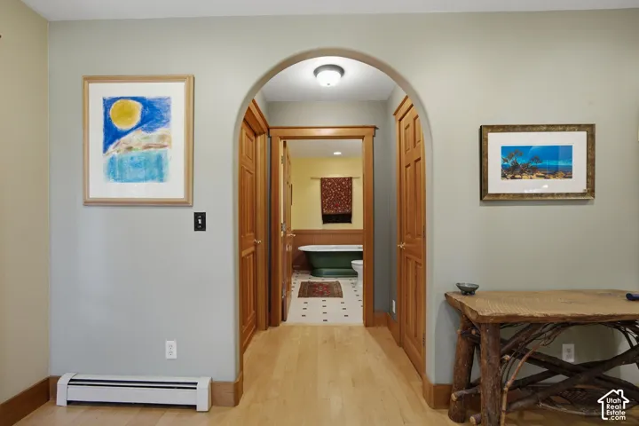 Wood-finish flooring, arched doorway with wood trim, wood paneled doors, baseboard heating unit, interior light fixture