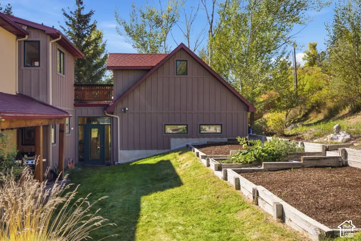 Board and batten exterior with a red roof, a covered patio, a second-story balcony, and terraced garden beds