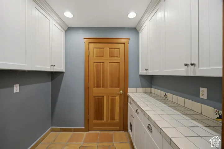 White shaker-style cabinetry with chrome hardware, tile countertop, tile flooring, wood-paneled door, and recessed lighting