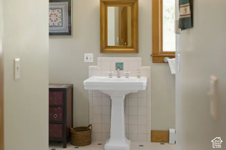 Pedestal sink with white tile backsplash, wood-framed mirror, and wood-framed window