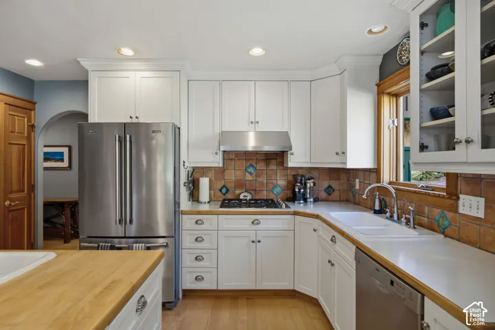 White cabinetry, stainless steel appliances, tile backsplash, wood-finish flooring, and a built-in sink