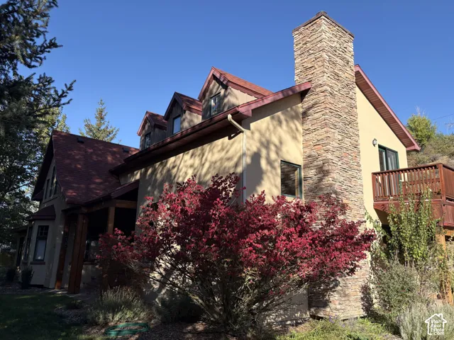 Stucco exterior with a stone-clad chimney and a red shingle roof