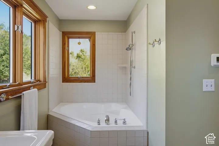 Corner soaking tub with tiled surround, polished chrome fixtures, and a wall-mounted shower head