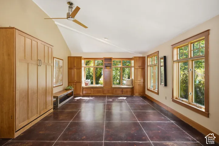 Vaulted ceiling with a ceiling fan, wood-frame windows, built-in window seating, integrated cabinetry, and large format floor tiling