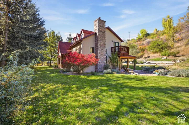 Expansive green lawn with mature evergreen trees, a stone-clad chimney, a red roof, and a wood-decked balcony