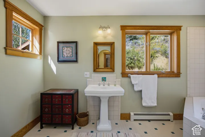 Pedestal sink with chrome fixtures, tiled flooring, wood-framed windows, and built-in bathtub