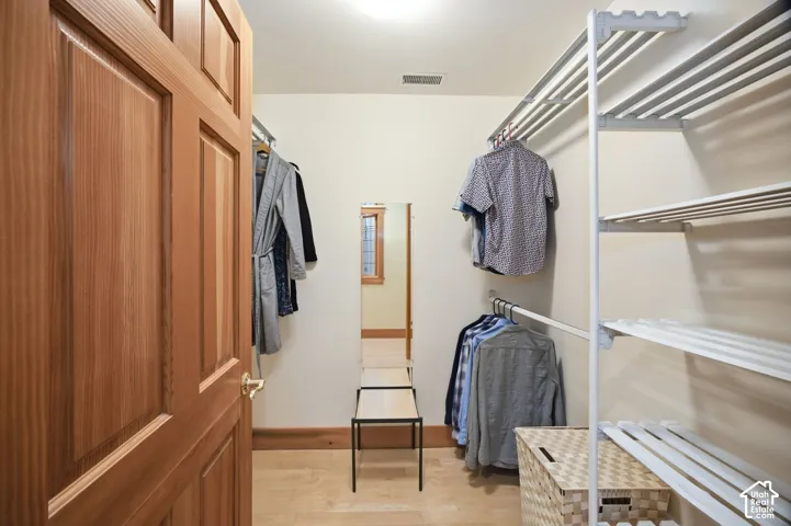 Walk-in closet with light wood paneled door, built-in shelving, hanging rods, and light wood-finish flooring