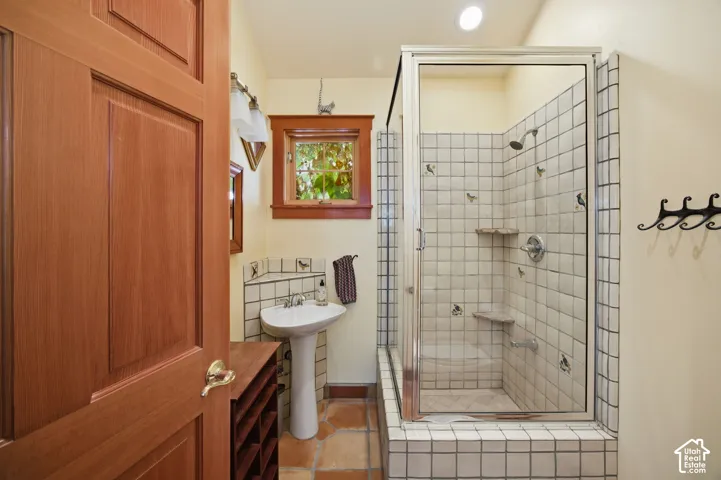 Pedestal sink with tiled backsplash, wood-framed window, and a shower enclosure featuring tiled walls, built-in shelves, and a clear glass door